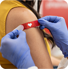 A provider wearing exam gloves places a bandage on the arm of a patient after a vaccination.